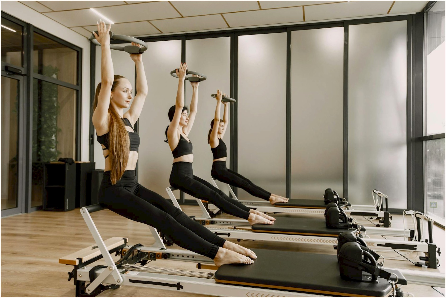 Three women synchronously practicing Pilates on reformers in a modern gym studio.