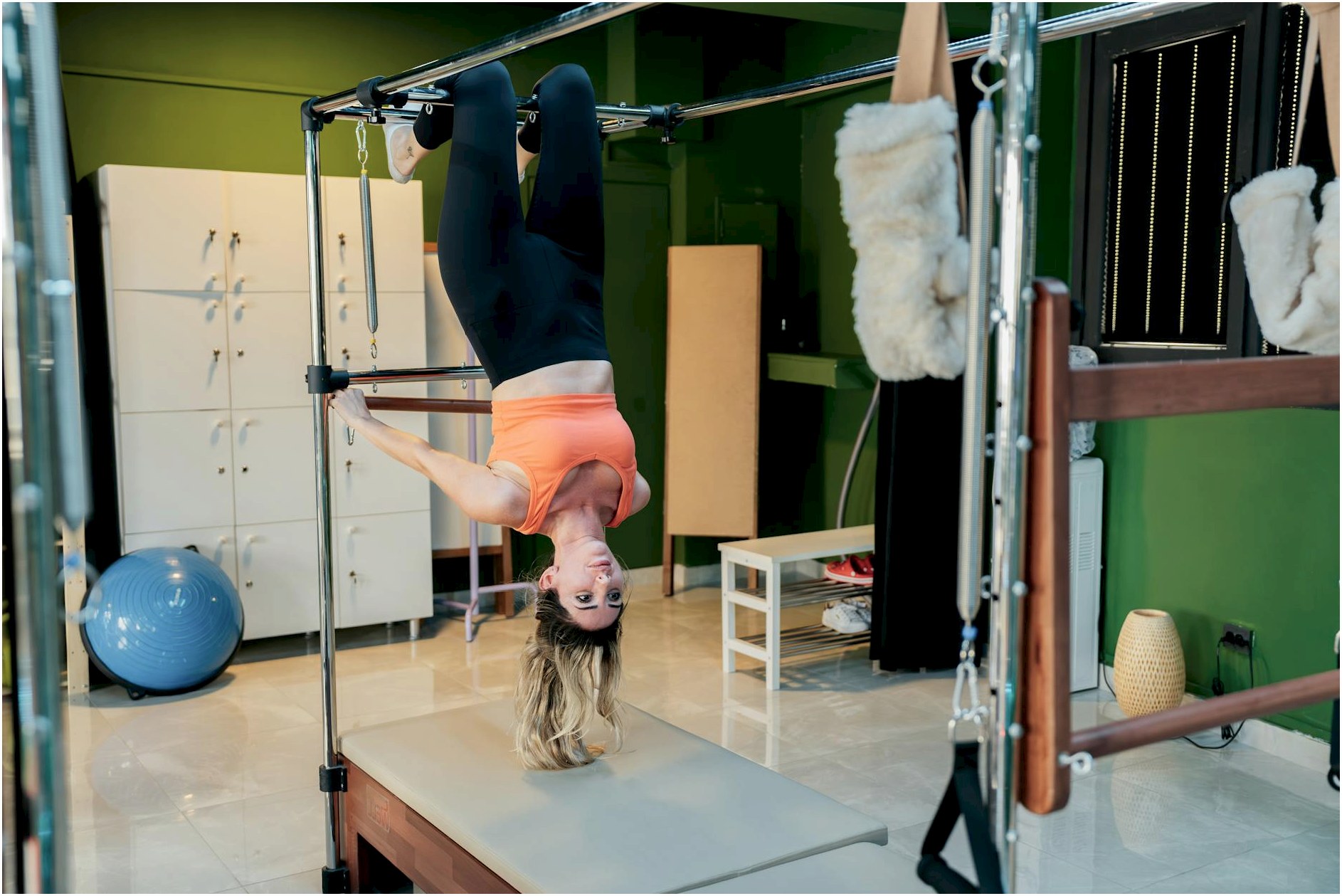Adult woman doing an upside-down pose on a reformer pilates machine in a fitness studio.