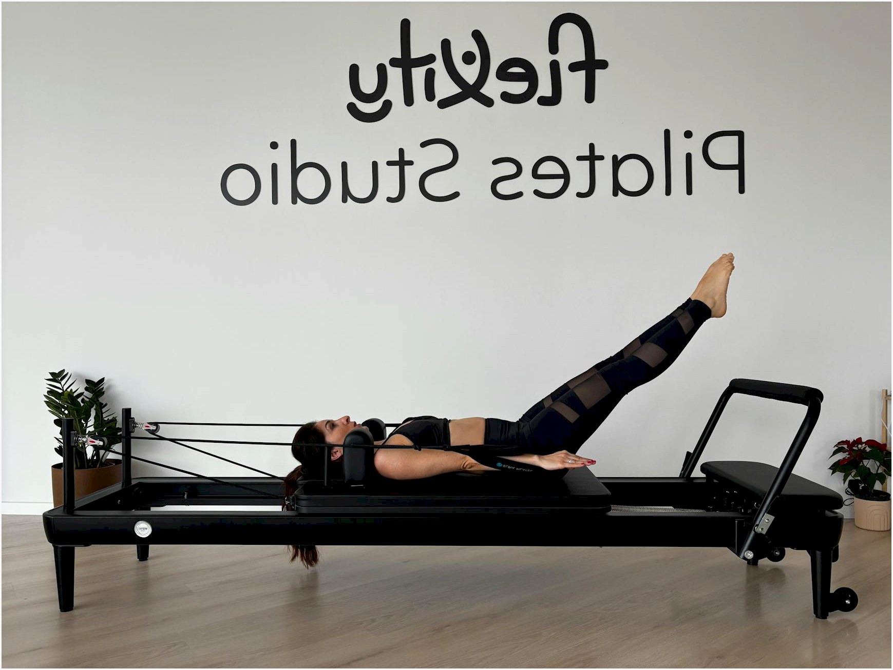 A woman performing Pilates exercises on a reformer in a modern fitness studio.