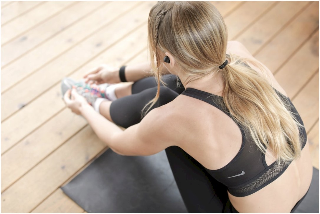 woman in black sports bra and black leggings sitting on brown wooden floor