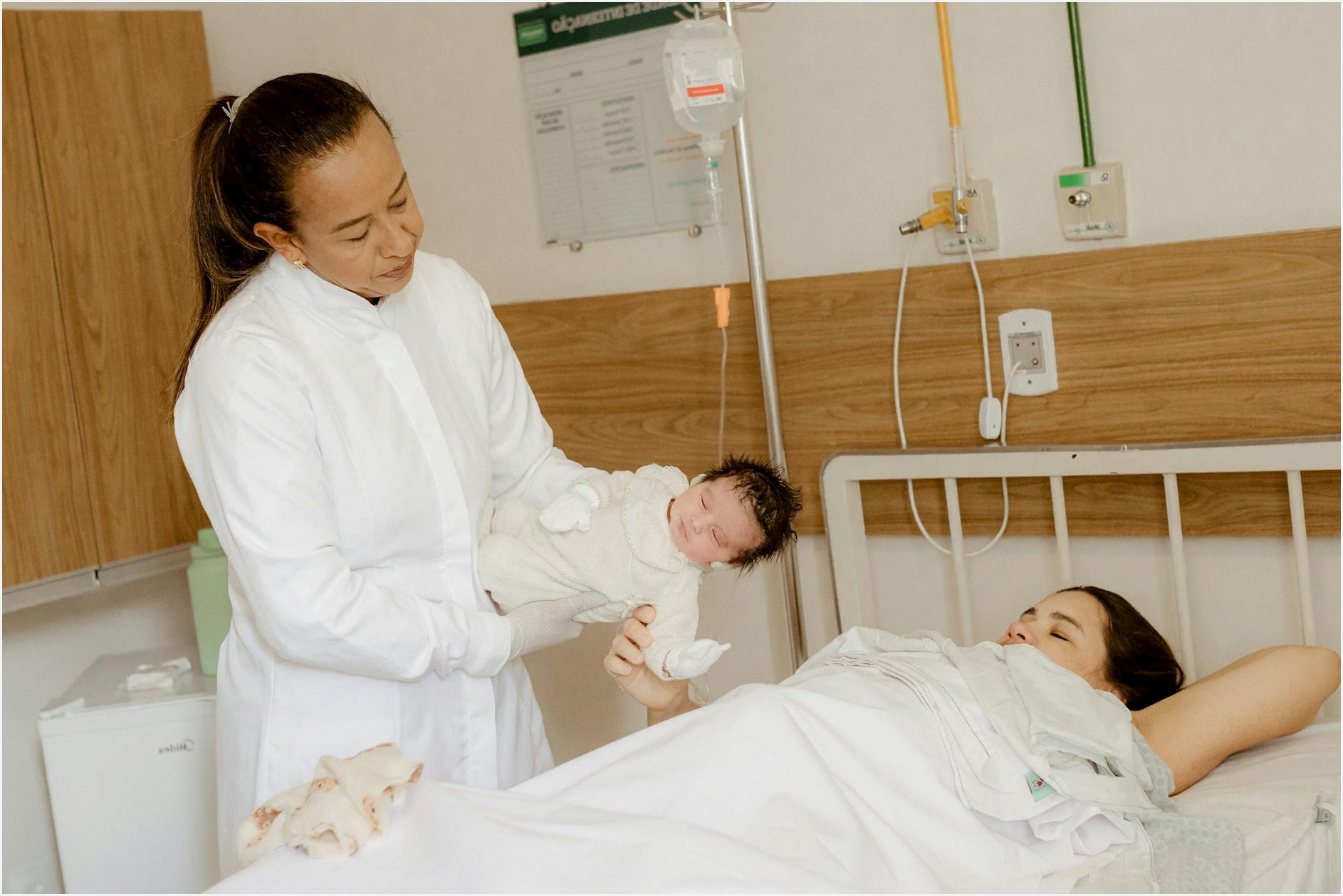 A doctor assists a new mother with her newborn baby in a hospital room setting.