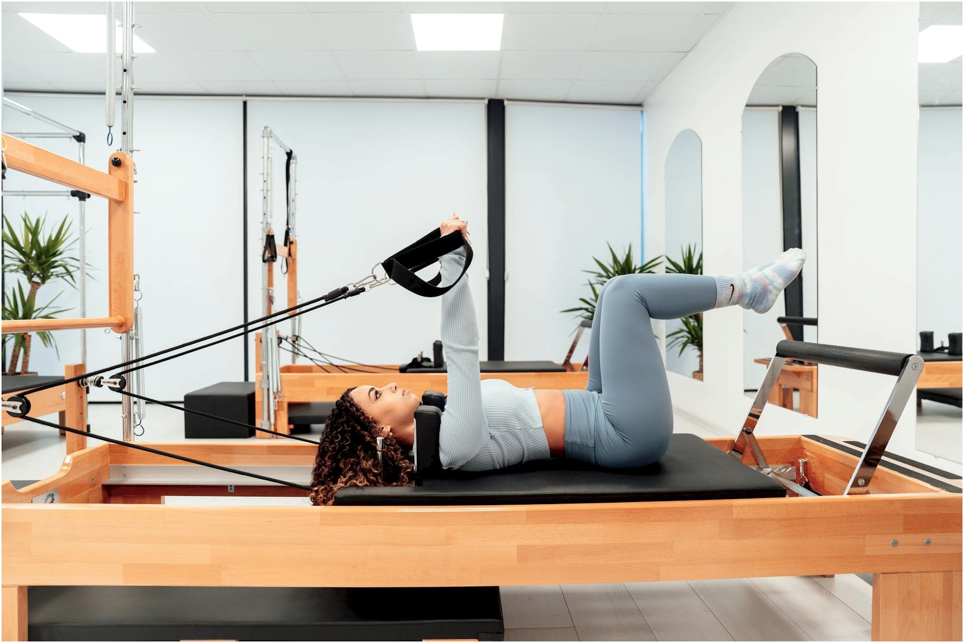 Woman working out on a Pilates reformer in a modern, well-equipped gym for fitness and health.