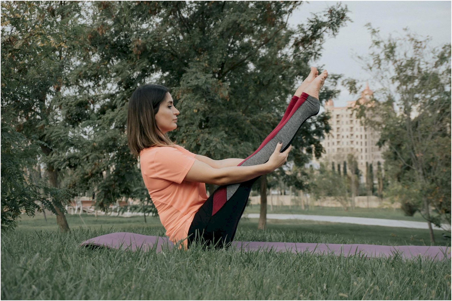 Woman practicing yoga outdoors, balancing in a yoga pose on a mat in a lush green park.