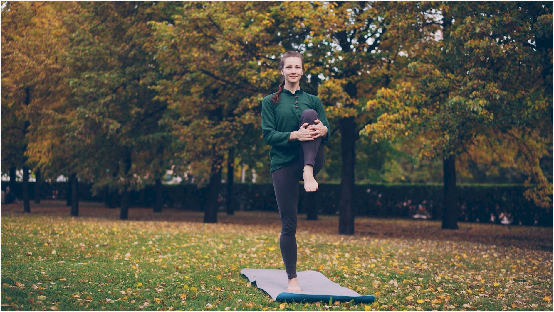 A woman practicing yoga on a mat in a park surrounded by autumn trees, promoting outdoor fitness.