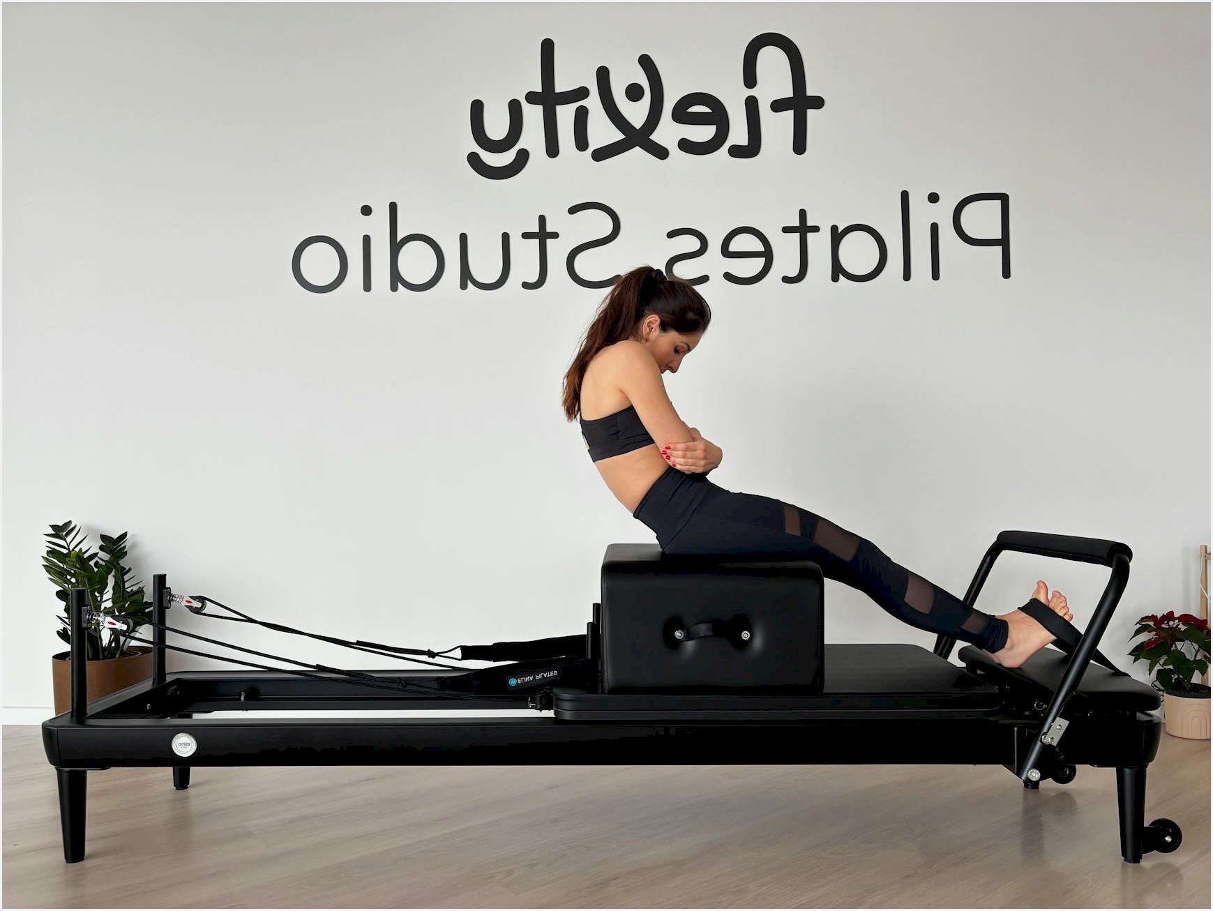 A woman is doing a Pilates workout on a reformer machine at a Pilates studio.