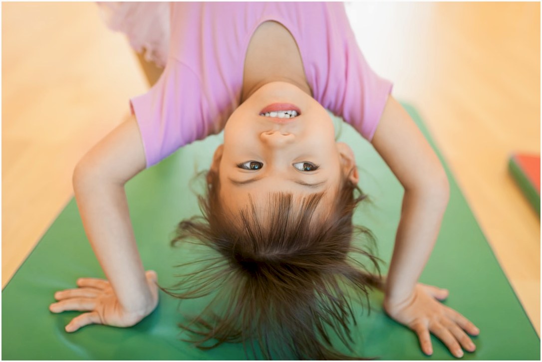 A young girl smiling upside down on a green mat.