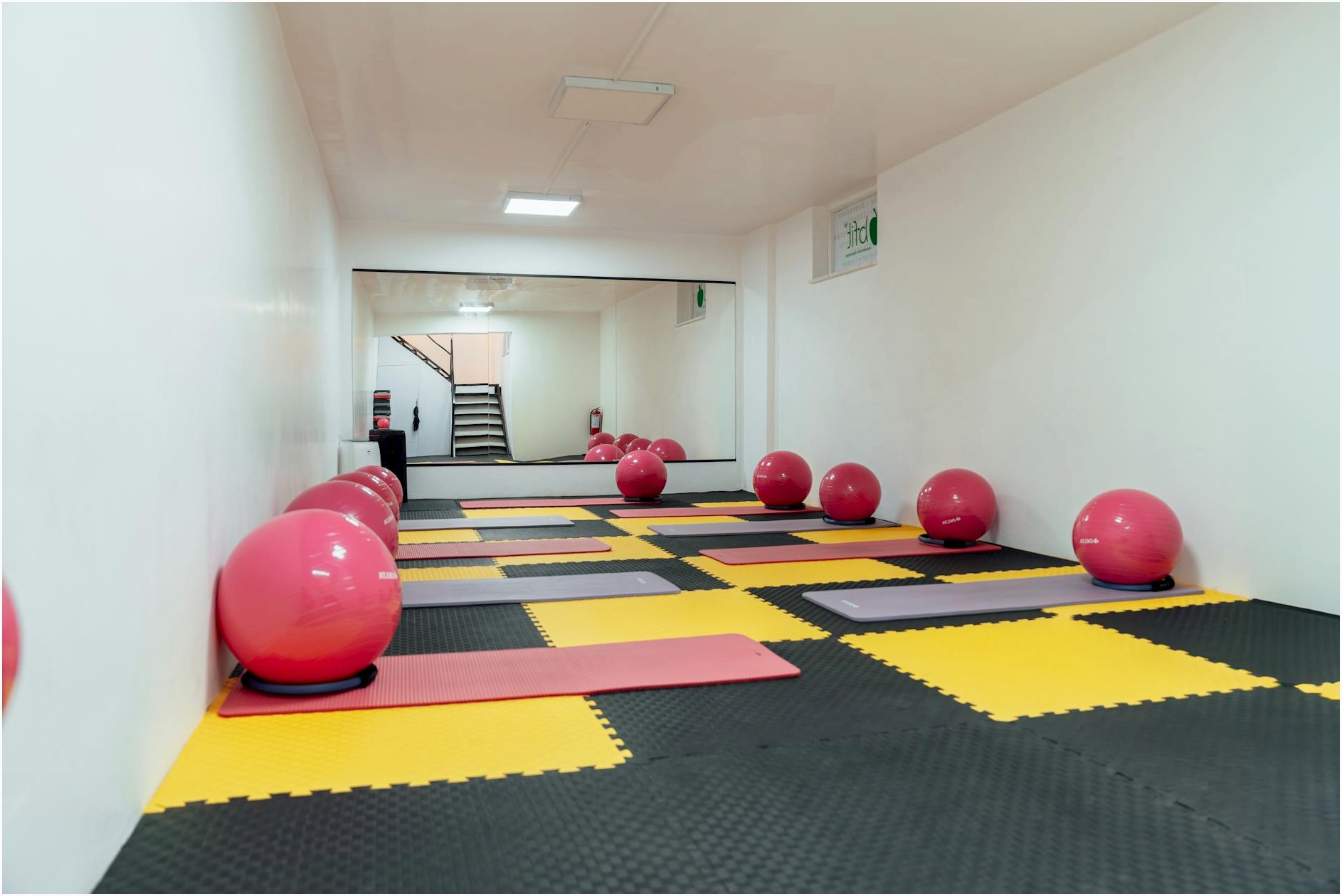 A modern gym interior featuring pink exercise balls and yellow mats, ideal for fitness classes.