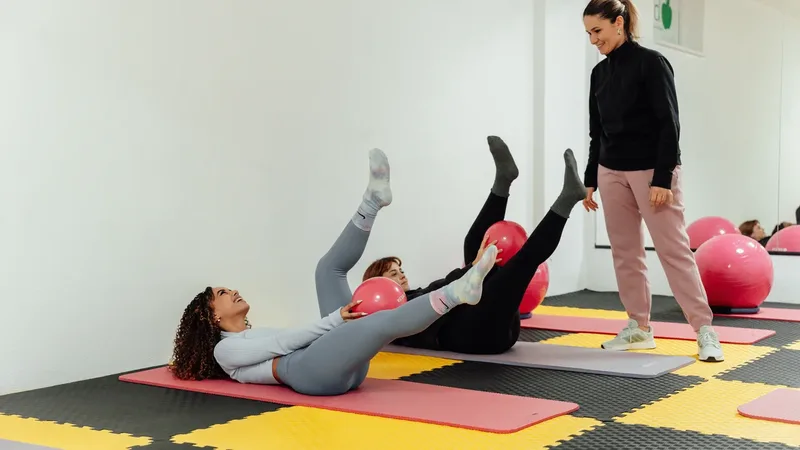 Instrutora orienta duas alunas durante exercício de Pilates em colchonetes com bolas de estabilidade