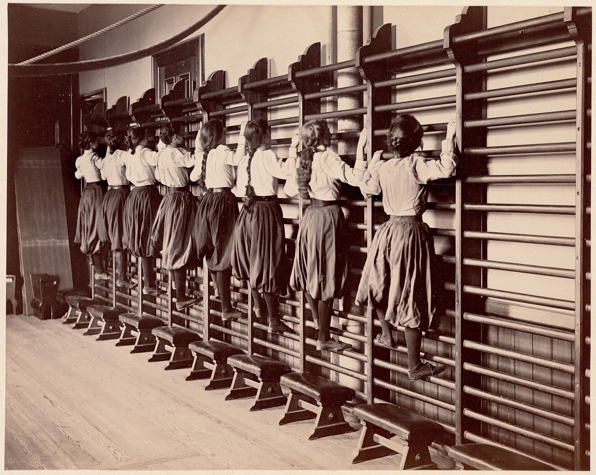 Grupo realizando exercícios em barras fixadas à parede; imagem histórica ilustrativa do espaldar.
