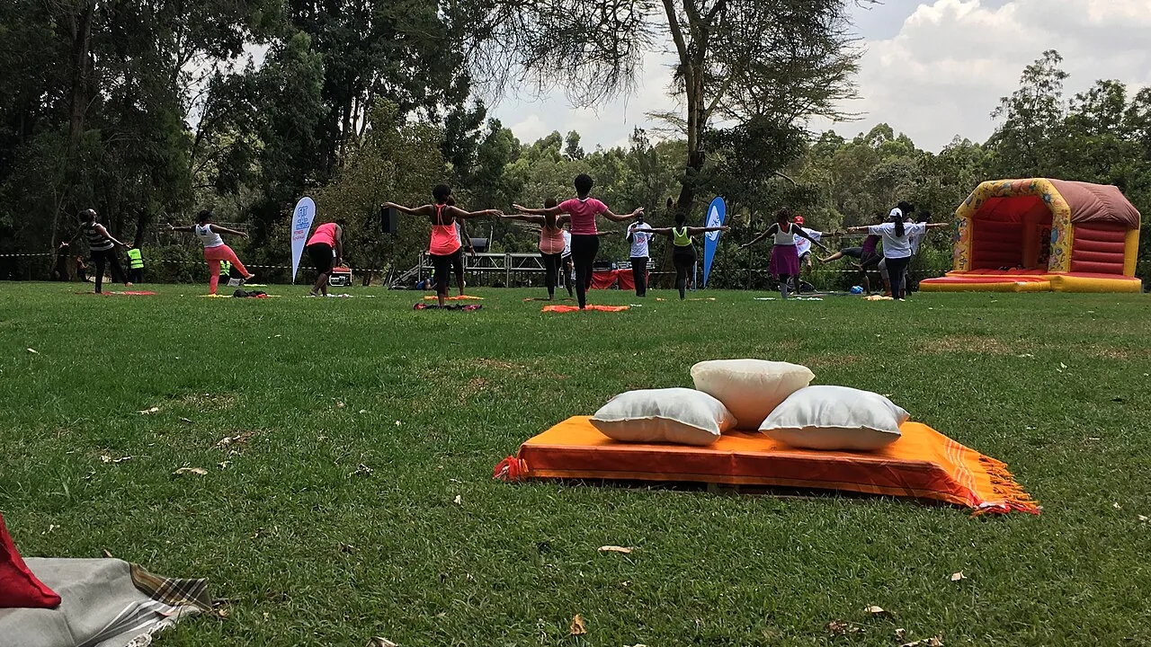Pessoas praticam movimentos de Pilates em grupo ao ar livre, em uma área arborizada.