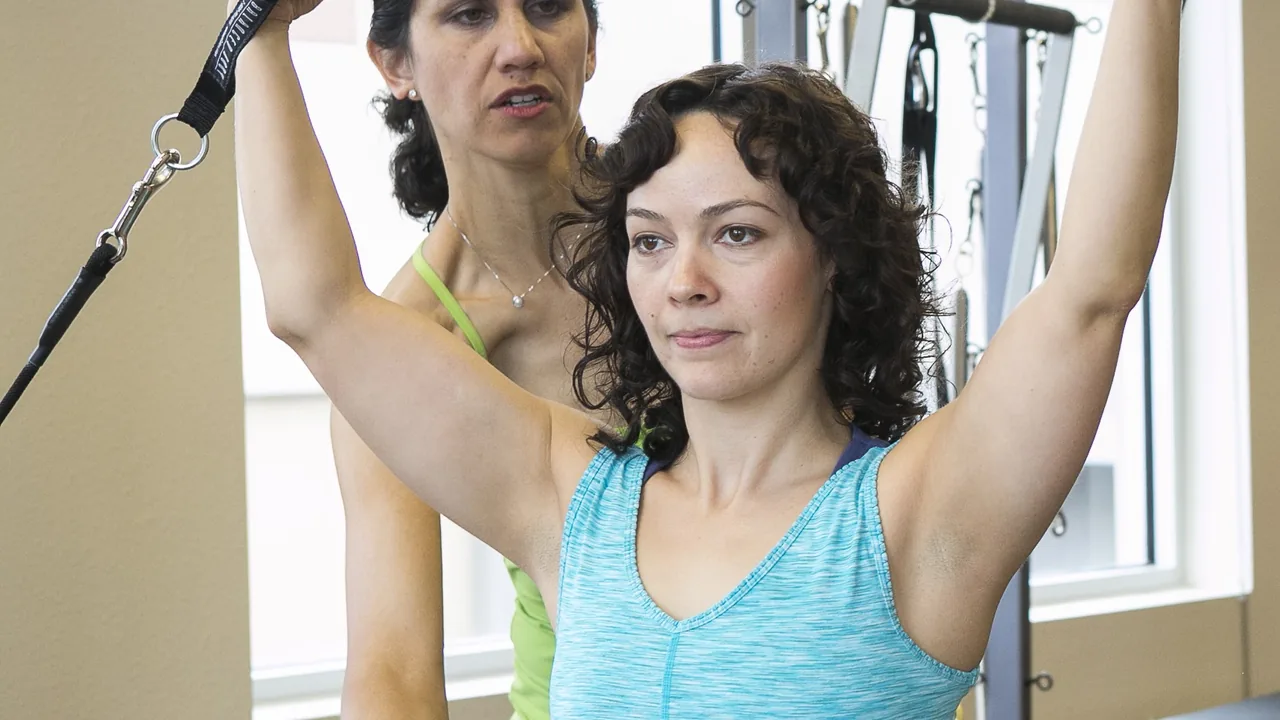 Instrutora orienta aluna em aparelho de Pilates em um estúdio