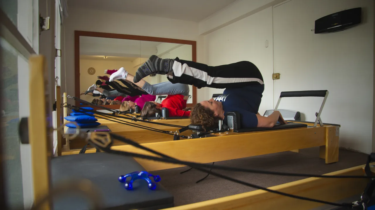 Aula de Pilates em aparelhos Reformer, com alunos deitados e pernas elevadas em um estúdio