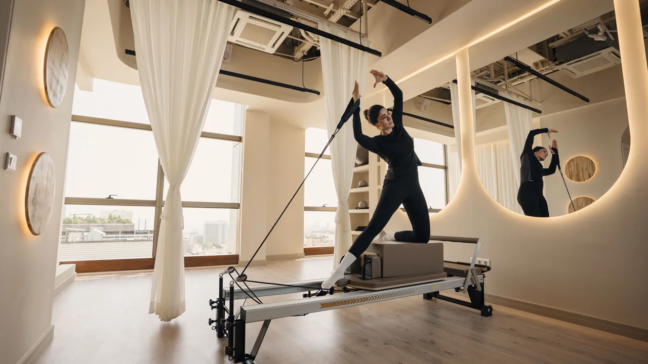 Reformer em um estúdio de Pilates iluminado, com uma praticante realizando um movimento controlado