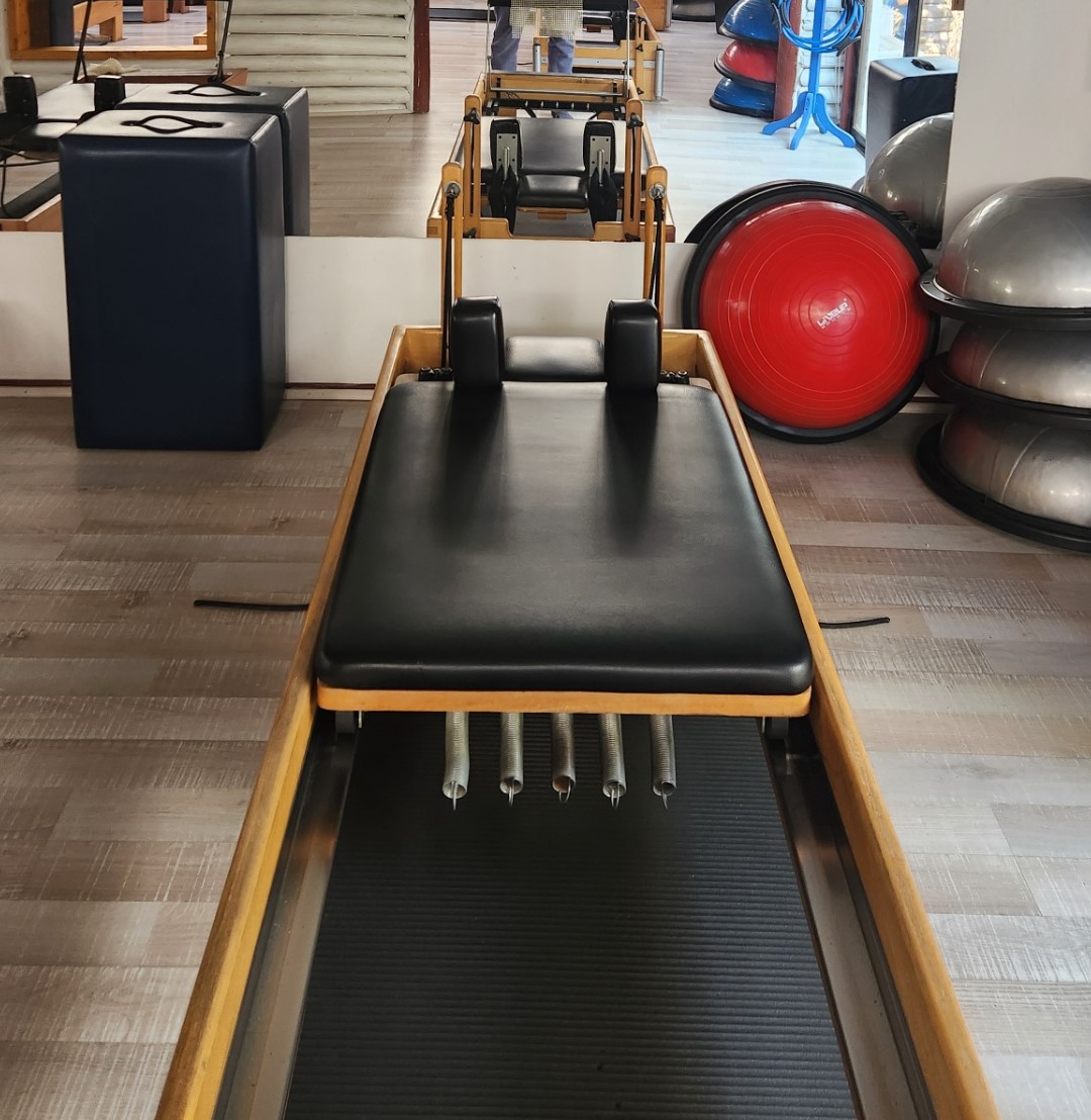 Aparelho Reformer de Pilates de madeira visto de frente em um estúdio, imagem ilustrativa para conferir modelo e encaixe.