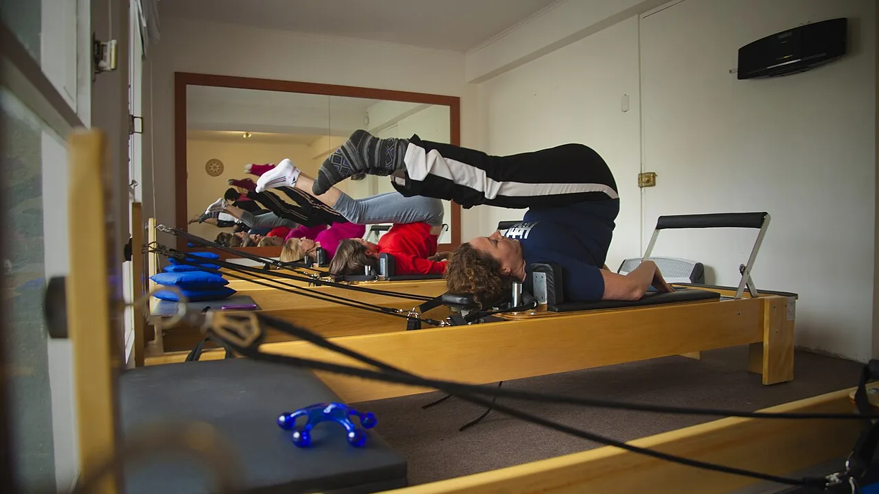 Aula de Pilates em aparelhos com praticantes realizando movimentos sob supervisão