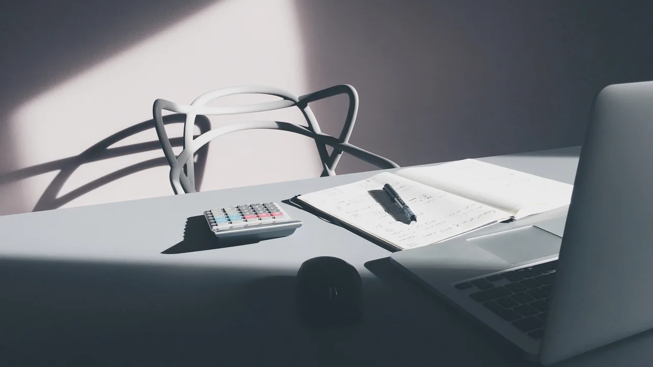 Calculadora, caderno e computador sobre uma mesa, usados como referência visual para calcular o preço de aulas de Pilates