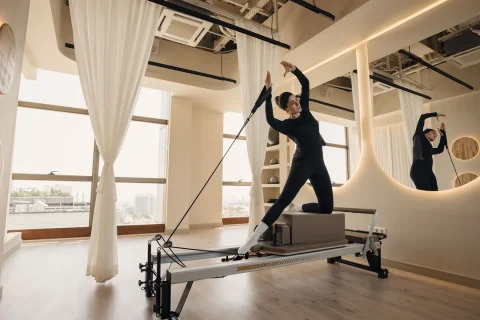 Pessoa praticando Pilates no Reformer em um estúdio iluminado.