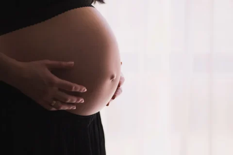 Gestante em perfil, com as mãos sobre a barriga, imagem destacada de artigo sobre Pilates no primeiro trimestre.