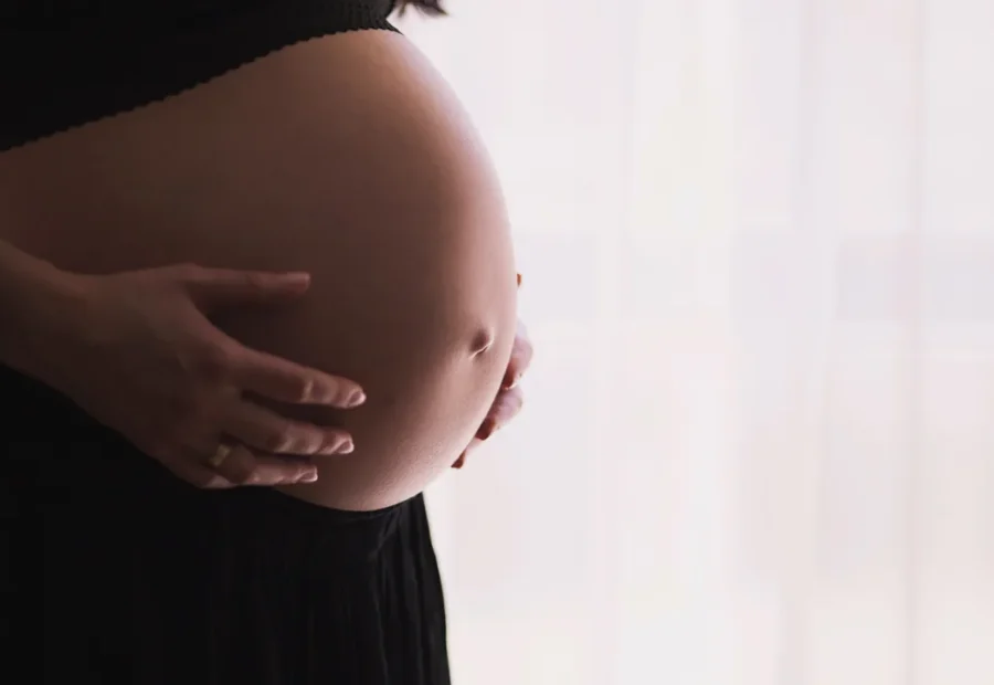 Gestante em perfil, com as mãos sobre a barriga, imagem destacada de artigo sobre Pilates no primeiro trimestre.