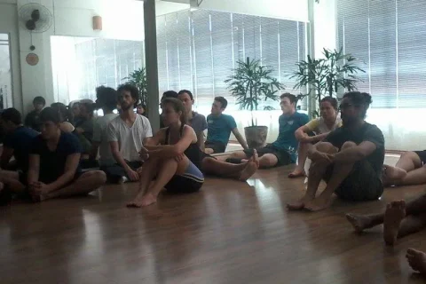 Aula coletiva de Pilates em estúdio, com participantes sentados no solo.