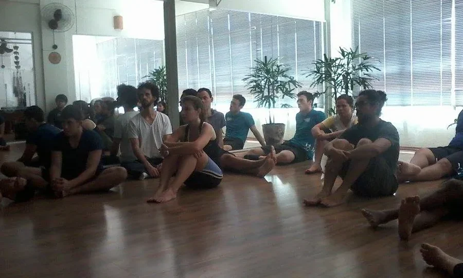 Aula coletiva de Pilates em estúdio, com participantes sentados no solo.