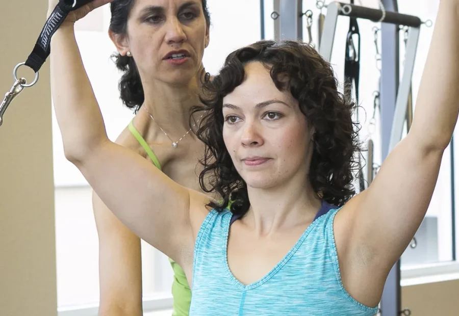 Instrutora orienta aluna em uma aula de Pilates com aparelho de suspensão.