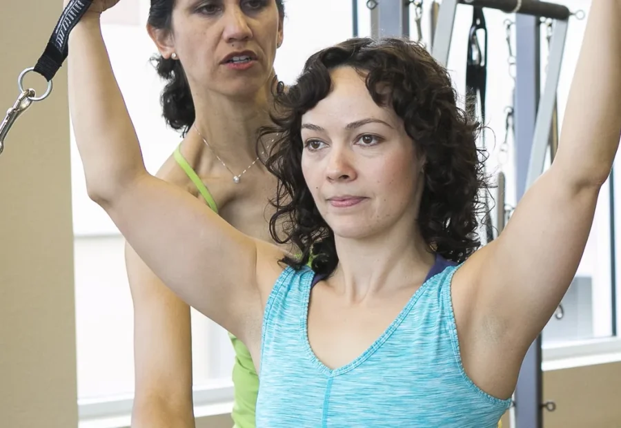 Pessoa praticando Pilates com orientação de uma instrutora em aparelho com alças.