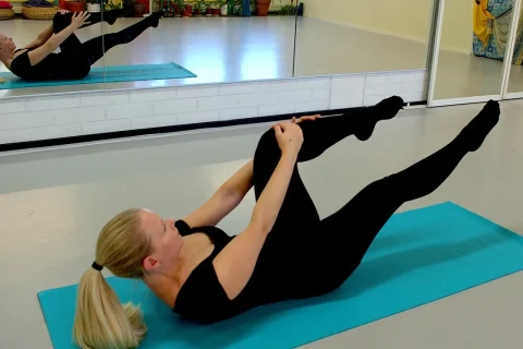 Pessoa praticando um movimento unilateral de Pilates no solo, com uma perna elevada e o tronco controlado.