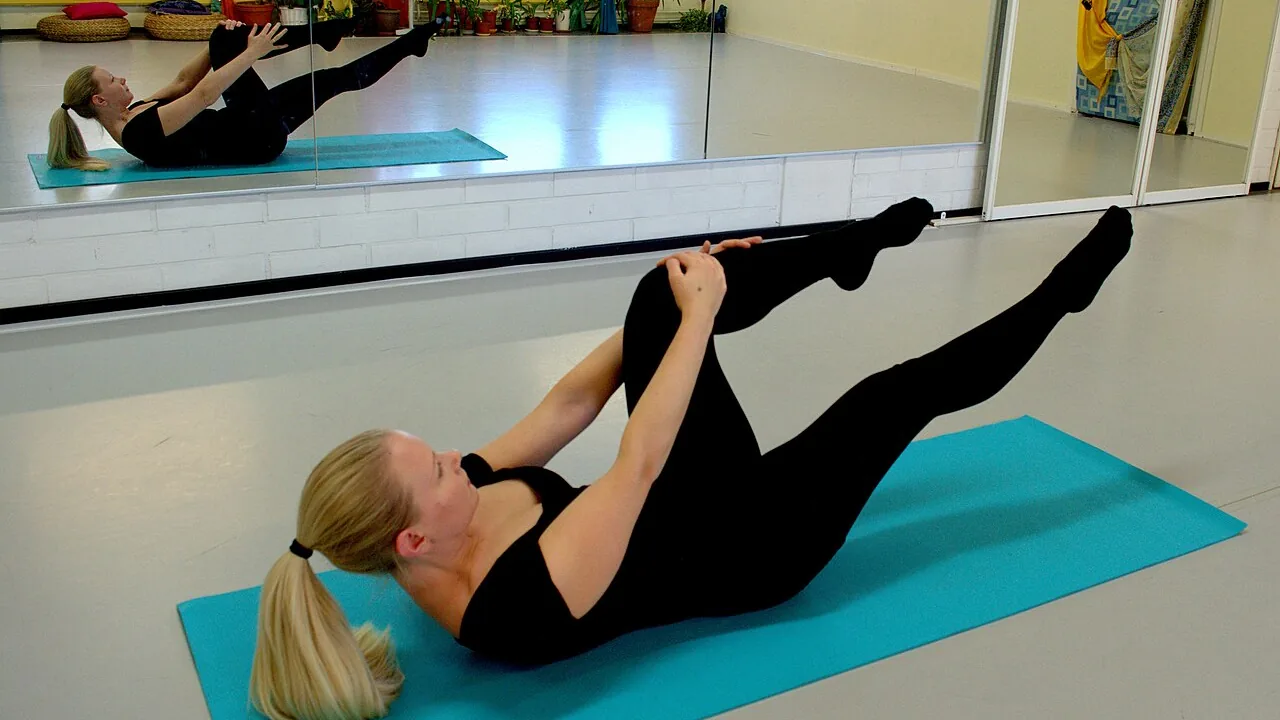 Pessoa praticando movimento unilateral de Pilates no solo, com uma perna elevada e o tronco controlado.