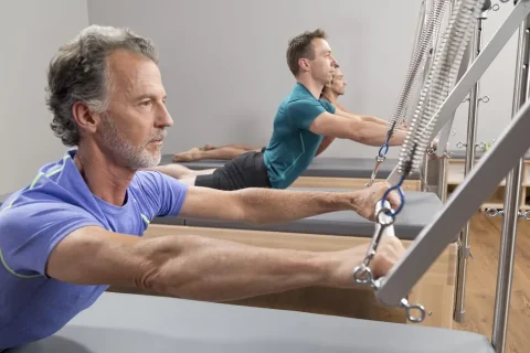 Pessoas praticando Pilates em Reformers com torre e molas