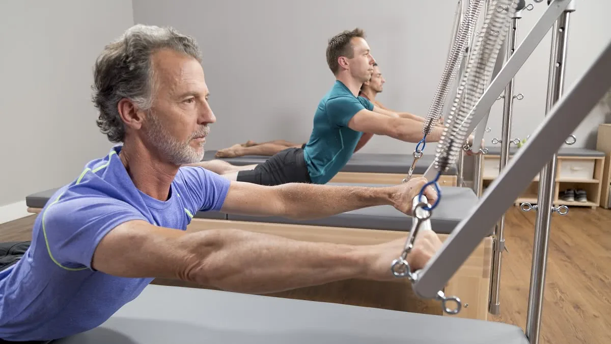Pessoas praticando Pilates em Reformers com torre e molas