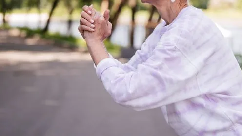 Mulher idosa faz um movimento leve durante atividade física ao ar livre