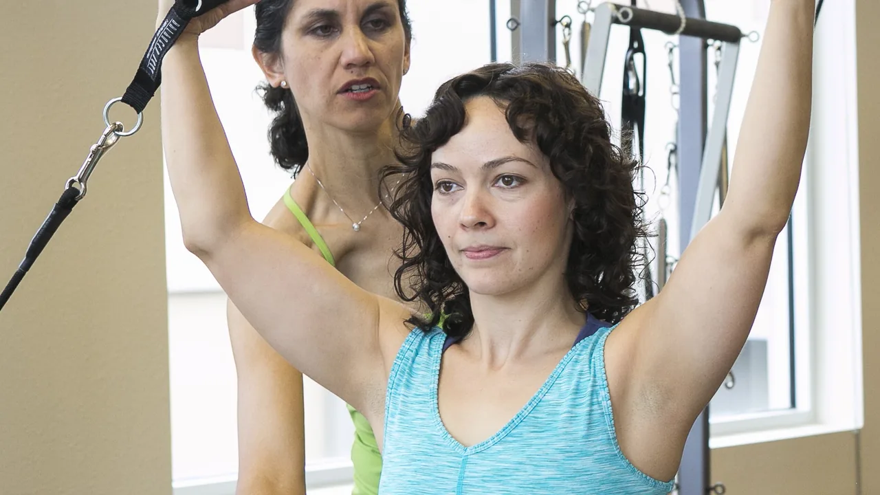 Instrutora orienta aluna durante exercício em um aparelho de Pilates