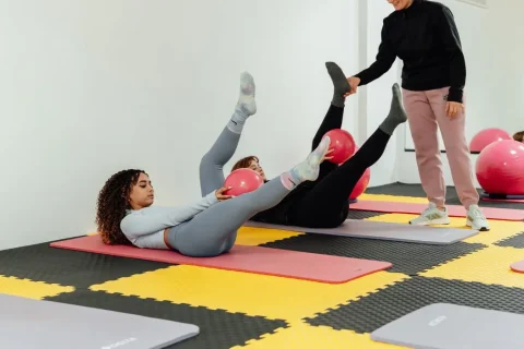 Aula de Pilates no solo com alunos executando exercícios com bolas sob supervisão