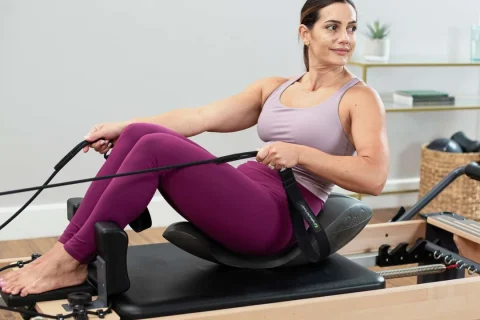 Pessoa sentada sobre o Oov em um Reformer de Pilates