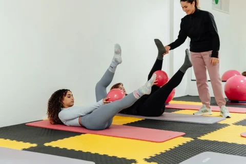 Aula de Pilates no solo com instrutora orientando alunas durante exercícios com bola