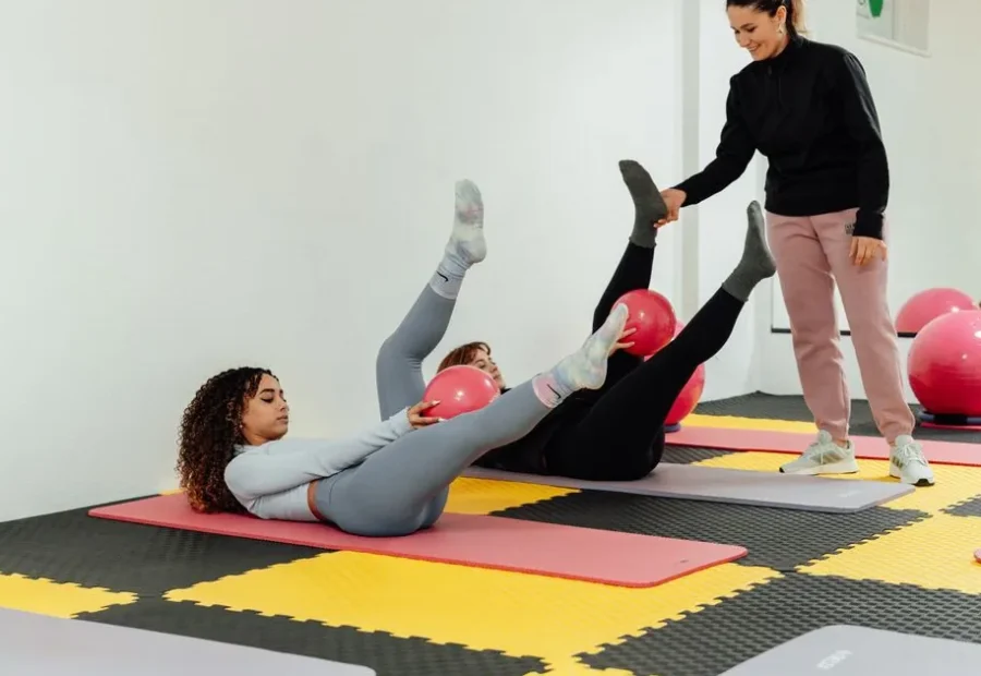 Aula de Pilates no solo com instrutora orientando alunas durante exercícios com bola
