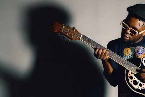 Músico tocando violão em pé, com o instrumento apoiado no corpo